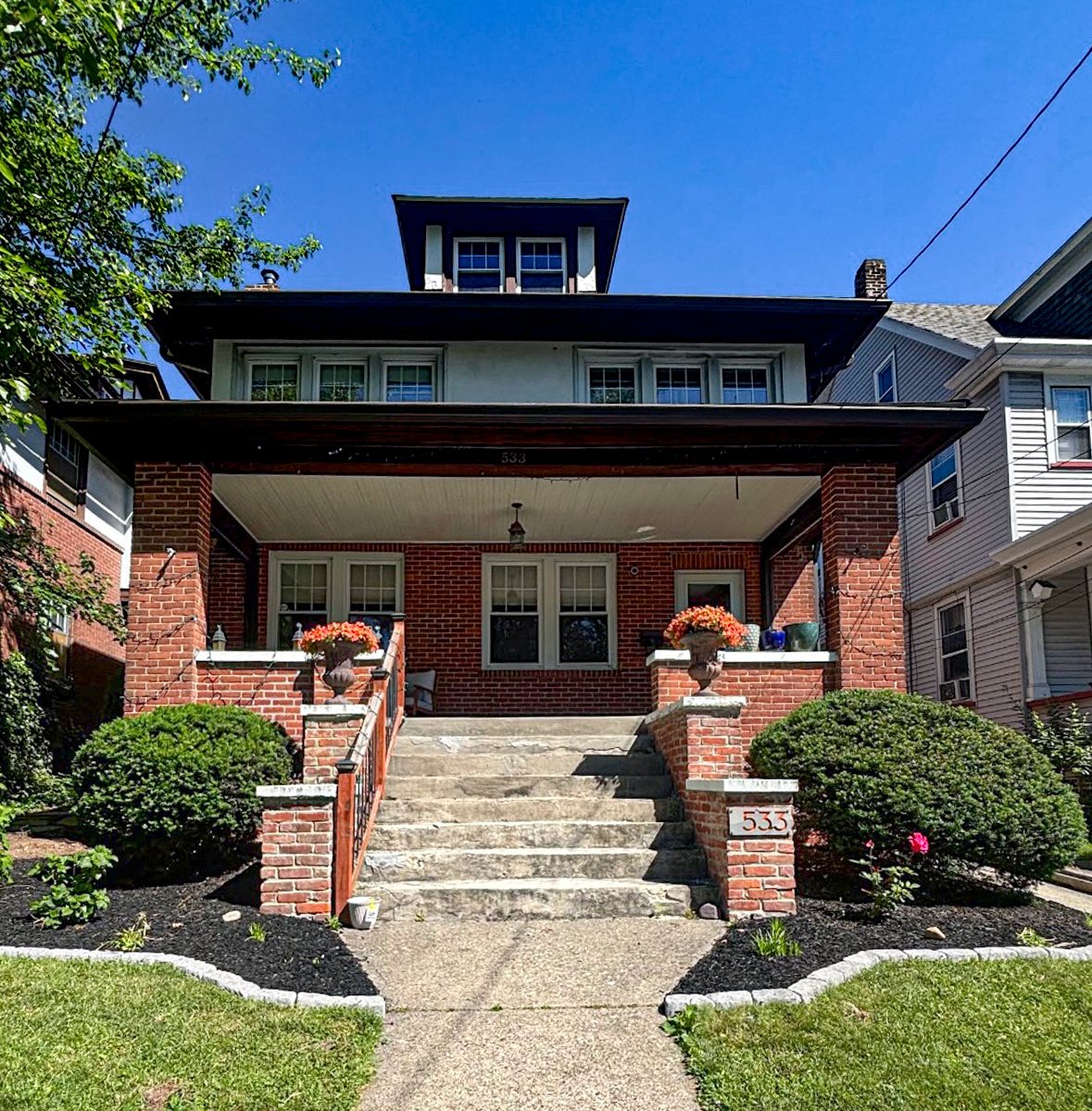 Classic brick foursquare home with tidy front landscaping and flower urns