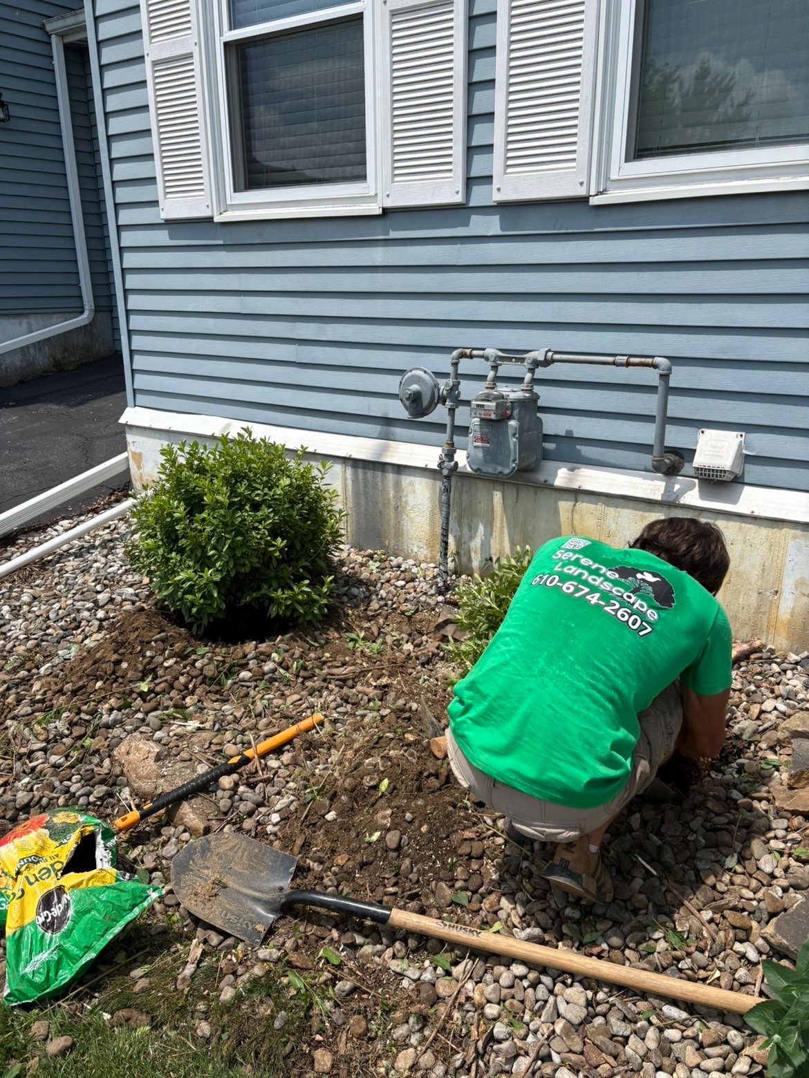 Team member planting a shrub in a fresh rock bed beside a home