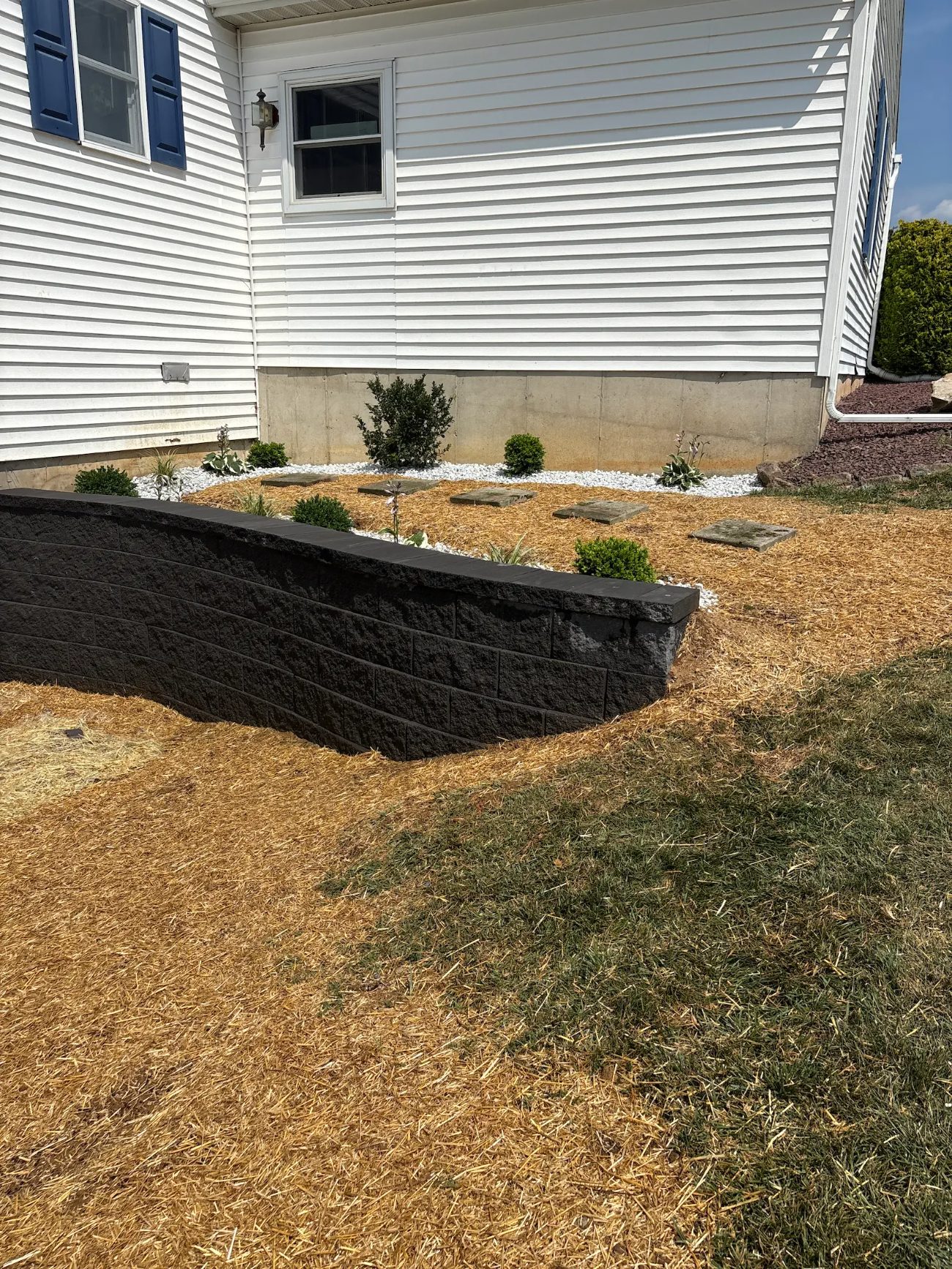 New charcoal block retaining wall with white rock bed and stepping stones